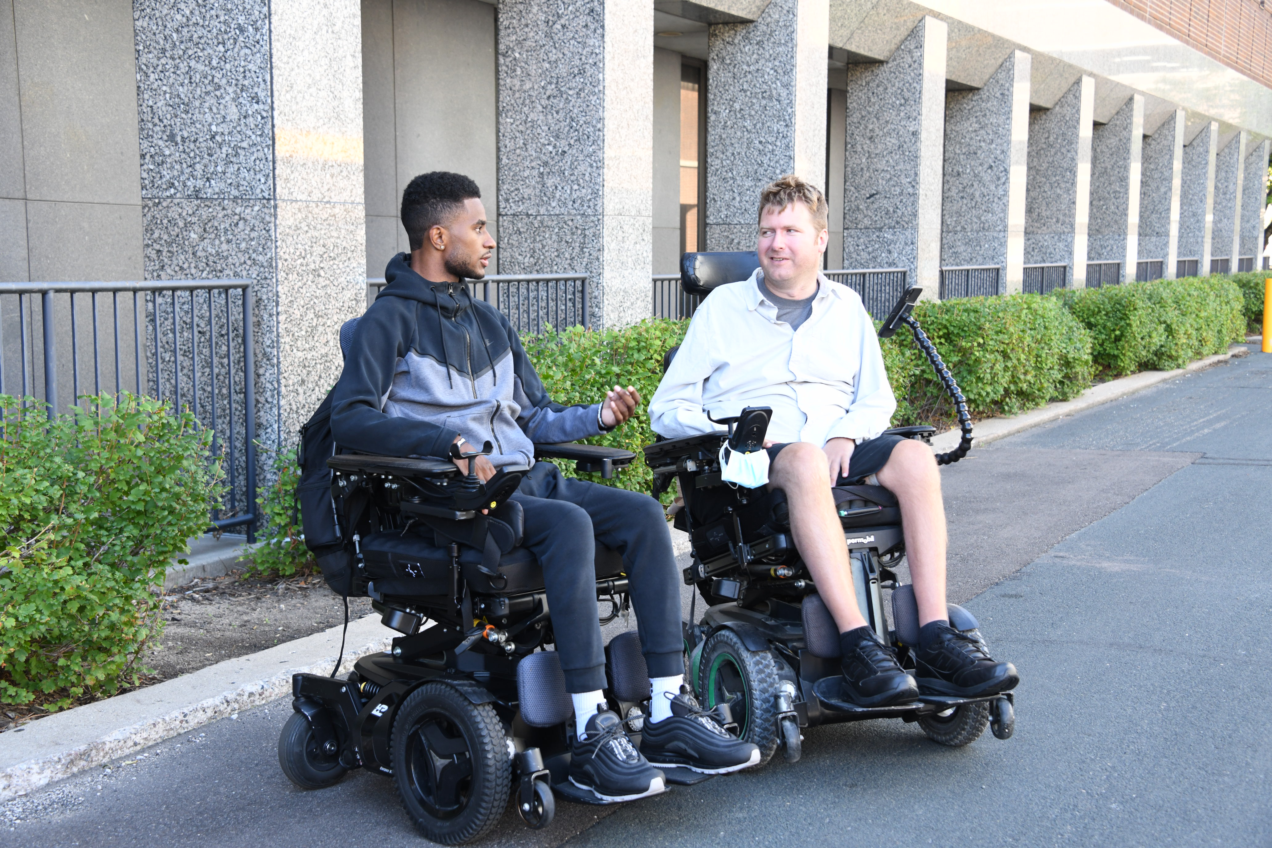 Two people with a spinal cord injury chatting outdoors on campus