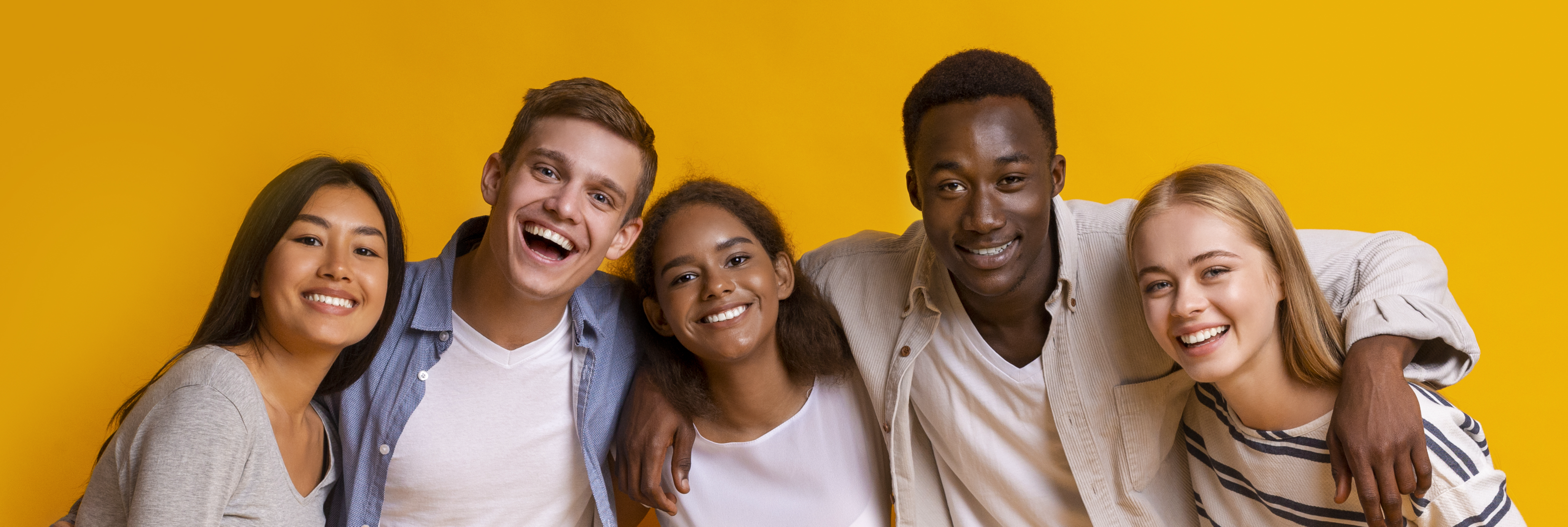 Friendly group of multiethnic students embracing and smiling over yellow background
