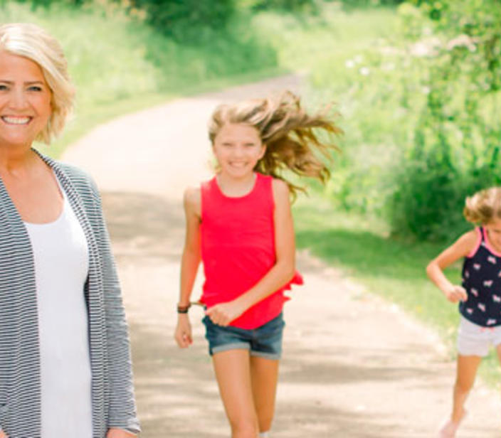 A woman looking at the camera with her two daughters running toward her