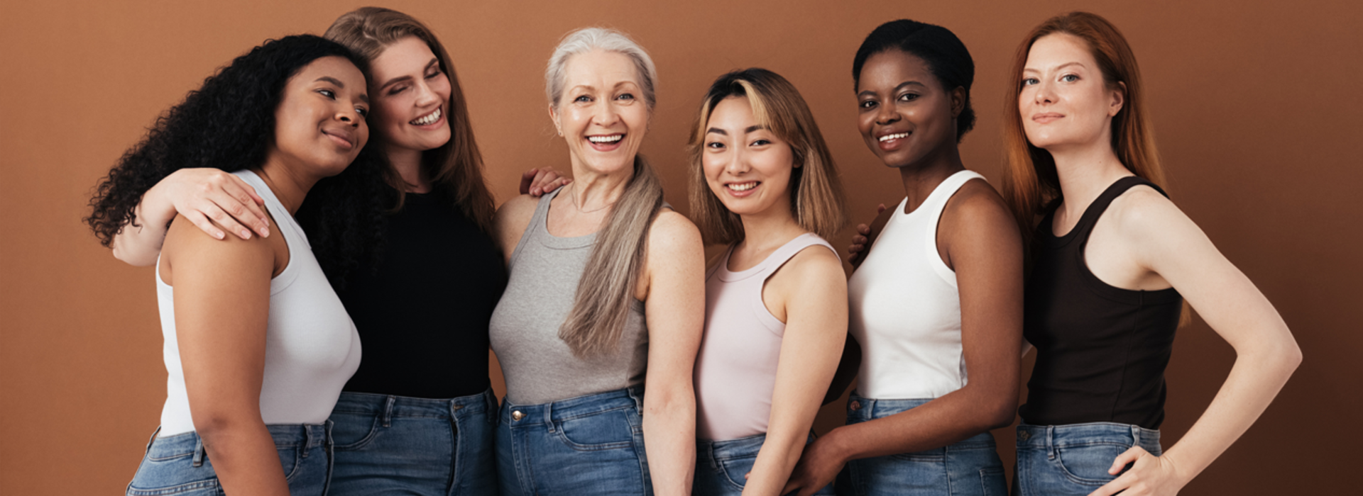 Group of women of different ages posing against brown background looking at camera
