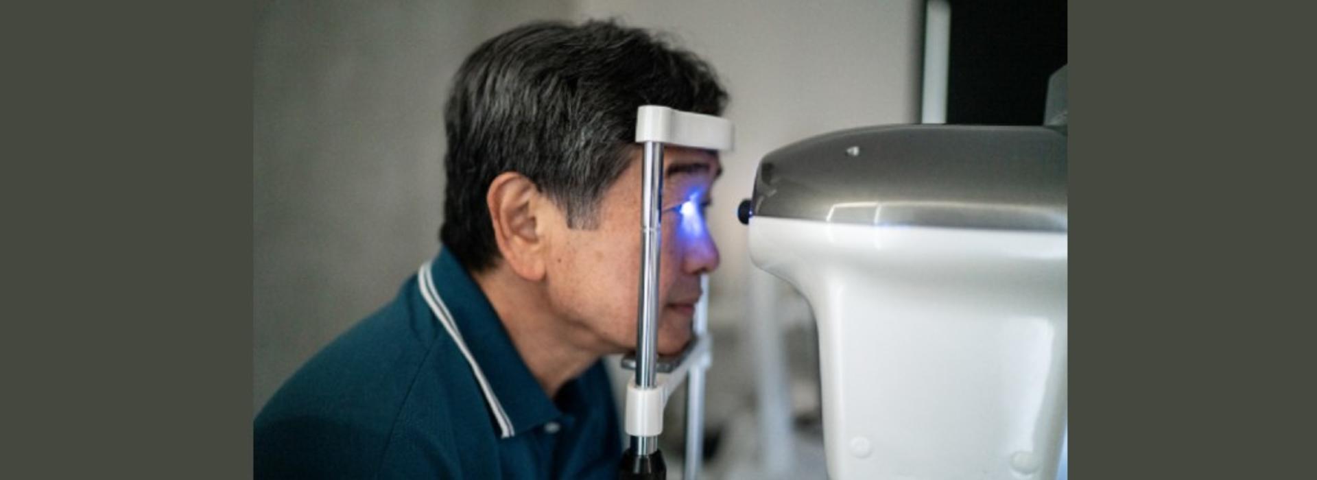 Man getting an eye scan, his head resting on a chin rest as a machine shines blue light into one of his eyes