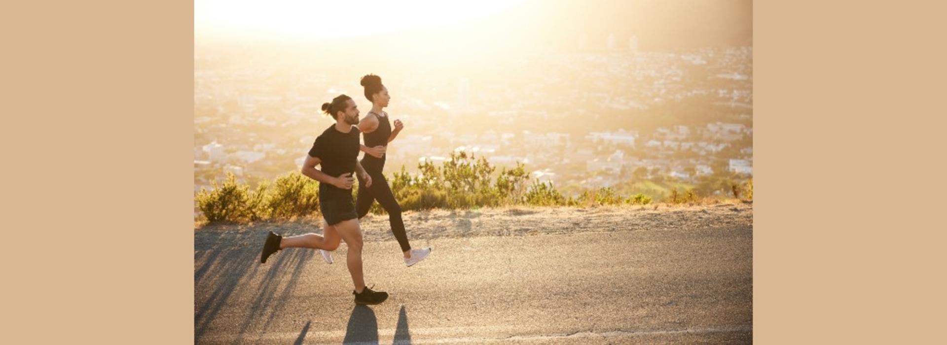 A man and woman running side-by-side down a road during sunrise. 
