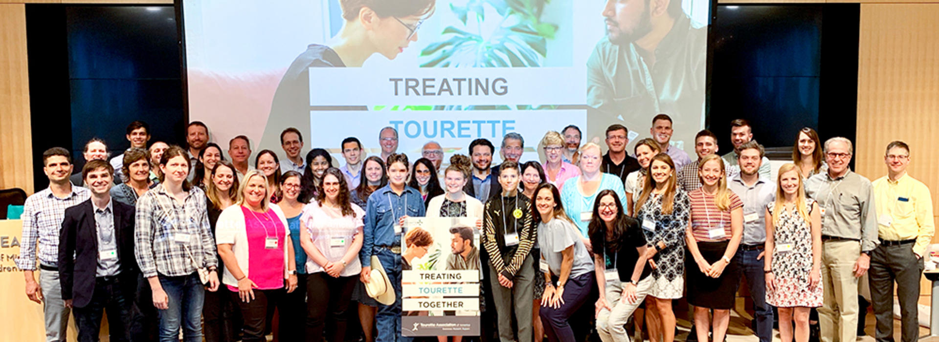 A group of people standing together in front of a sign saying Treating Tourette Together
