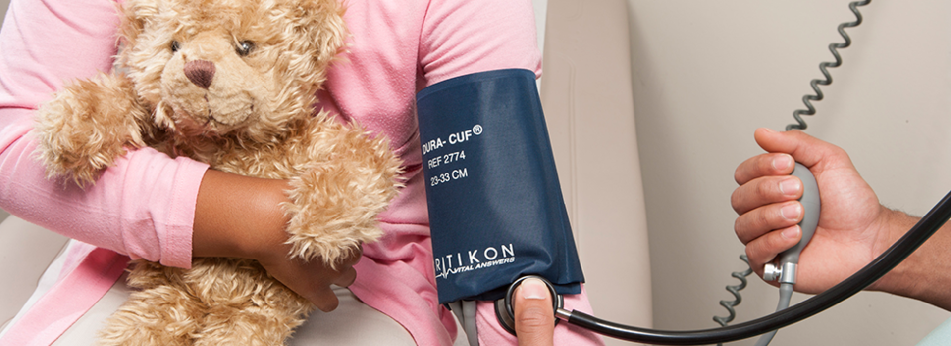 A young girl holding a teddy bear, getting her blood pressure taken.