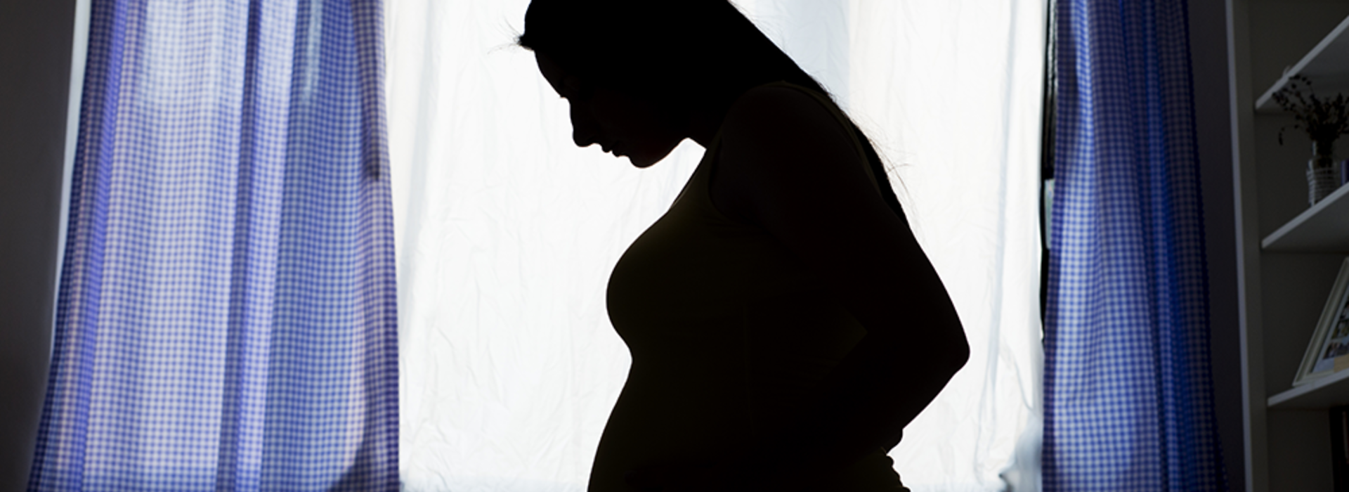 A silhouette of a pregnant woman in front of a large window.