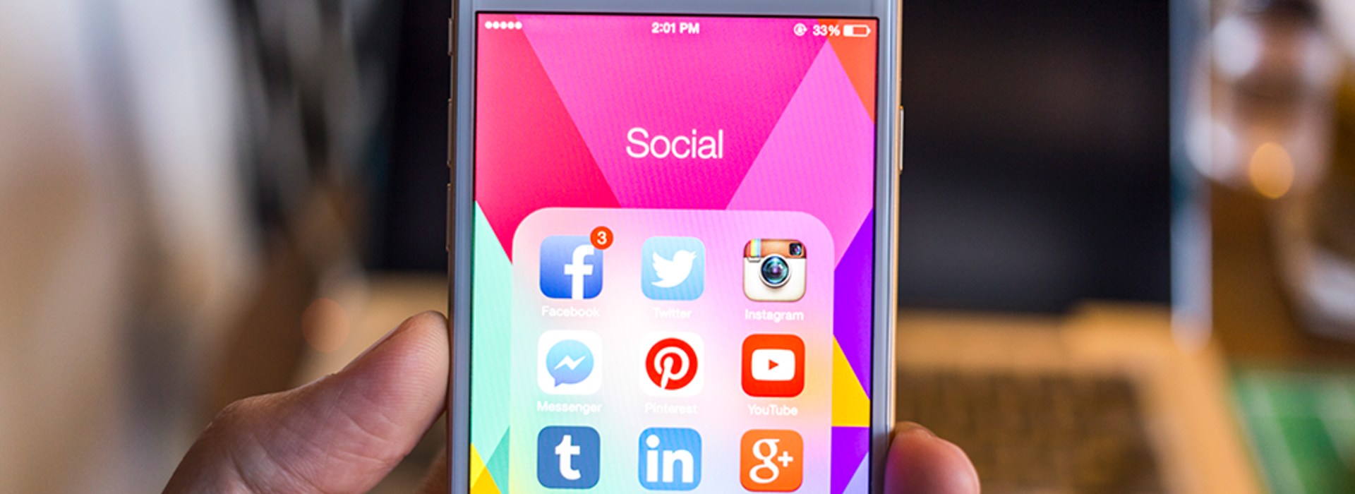 A hand holding a phone with social icons on the screen.