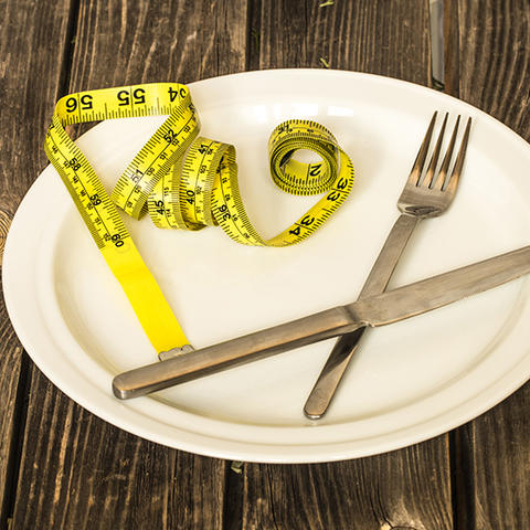 A plate on a wooden table with a fork and measurement tape on the plate.