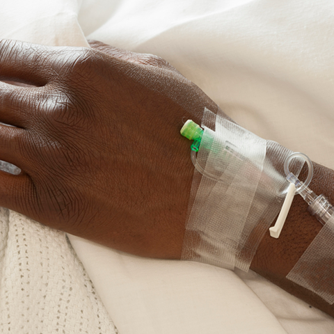 A close-up of a Black patient's hand with tape, hospital bands, and IVs.