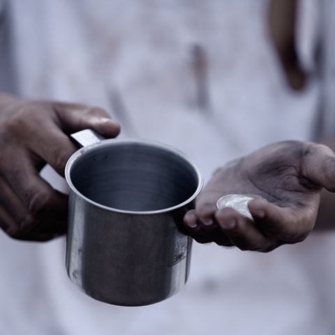 A Black man's hands holding a cup and coins.