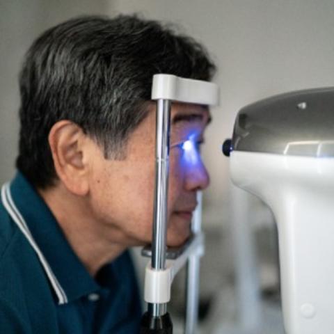 Man getting an eye scan, his head resting on a chin rest as a machine shines blue light into one of his eyes