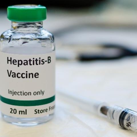 hepatitis B vaccine vial with syringe and stethoscope in the background