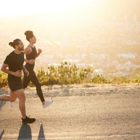 A man and woman running side-by-side down a road during sunrise. 