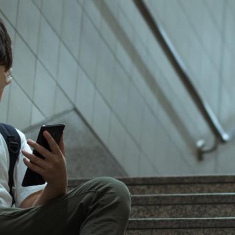 Child sitting on school steps looking at cell phone. 