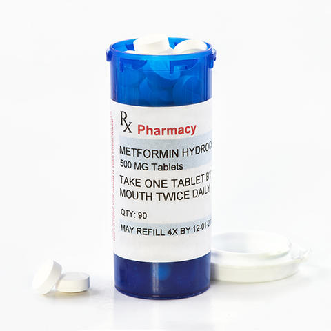 A pill bottle of metformin with the lid off and on the table.
